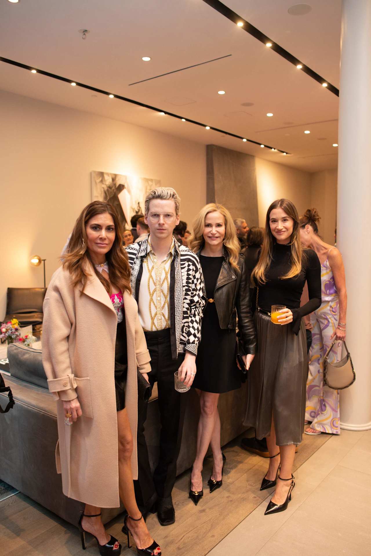 Five guests pose together at an indoor event, with other attendees gathered behind them.