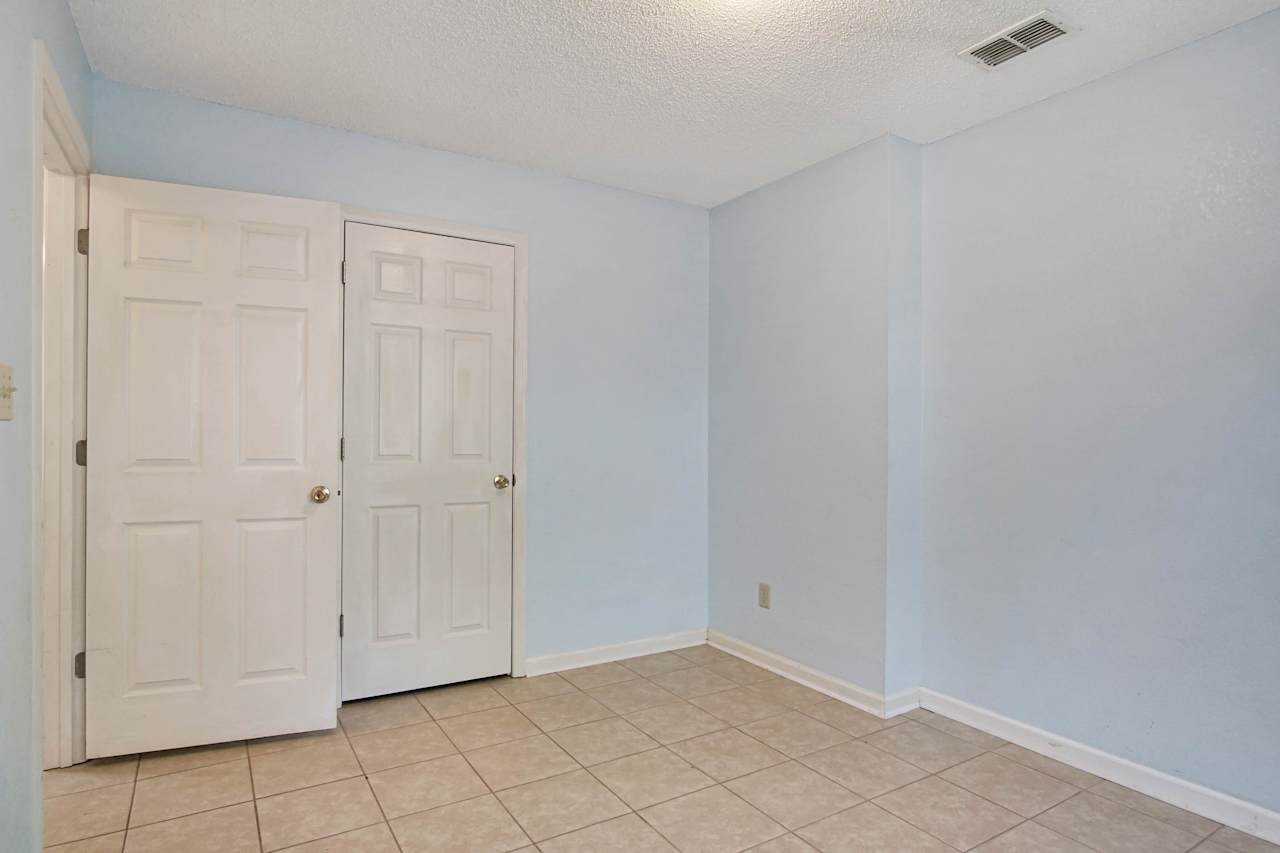 photo of second bedroom featuring light blue walls, white closet door, lightly colored tiled flooring, white ceilings, white baseboards, and the entrance to the main hallway