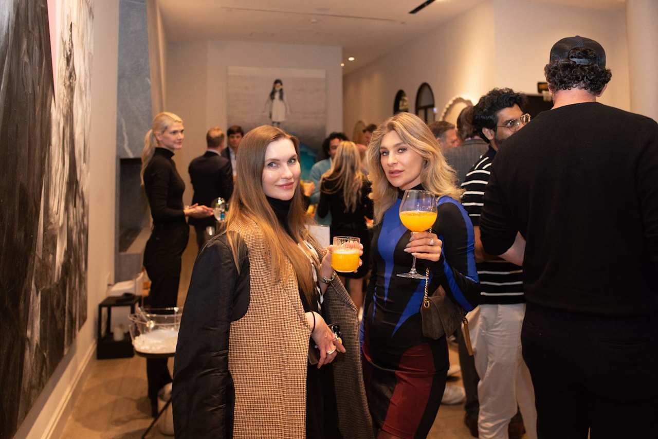 Guests mingle at an indoor reception; two women in the foreground hold drinks.