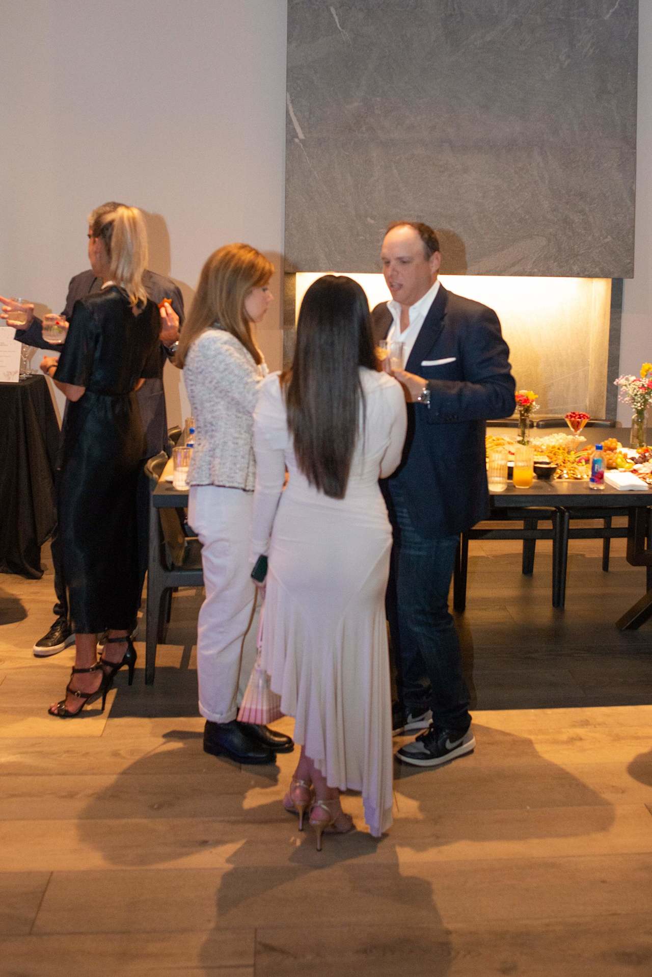 Guests mingle at a reception as a man in a navy suit talks with a woman in white.
