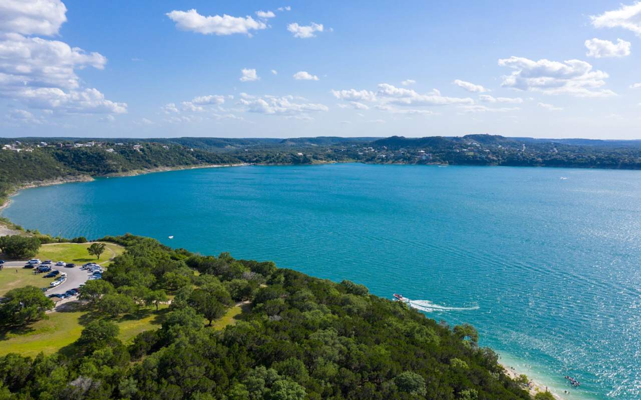 A large body of water surrounded by trees on a sunny day. The water is clear and blue, with few boats in the water.