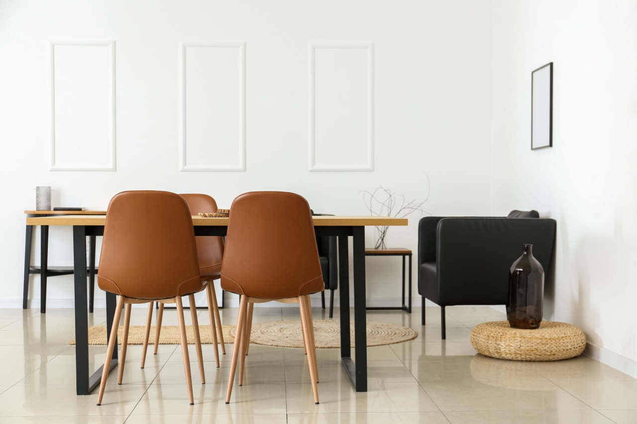 A dining room with a table, brown chairs, a black couch, and a vase.