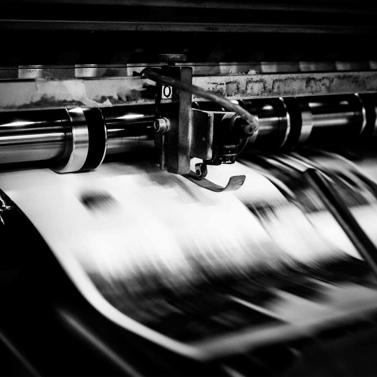 A black and white photo of a large printing press machine in a factory setting.