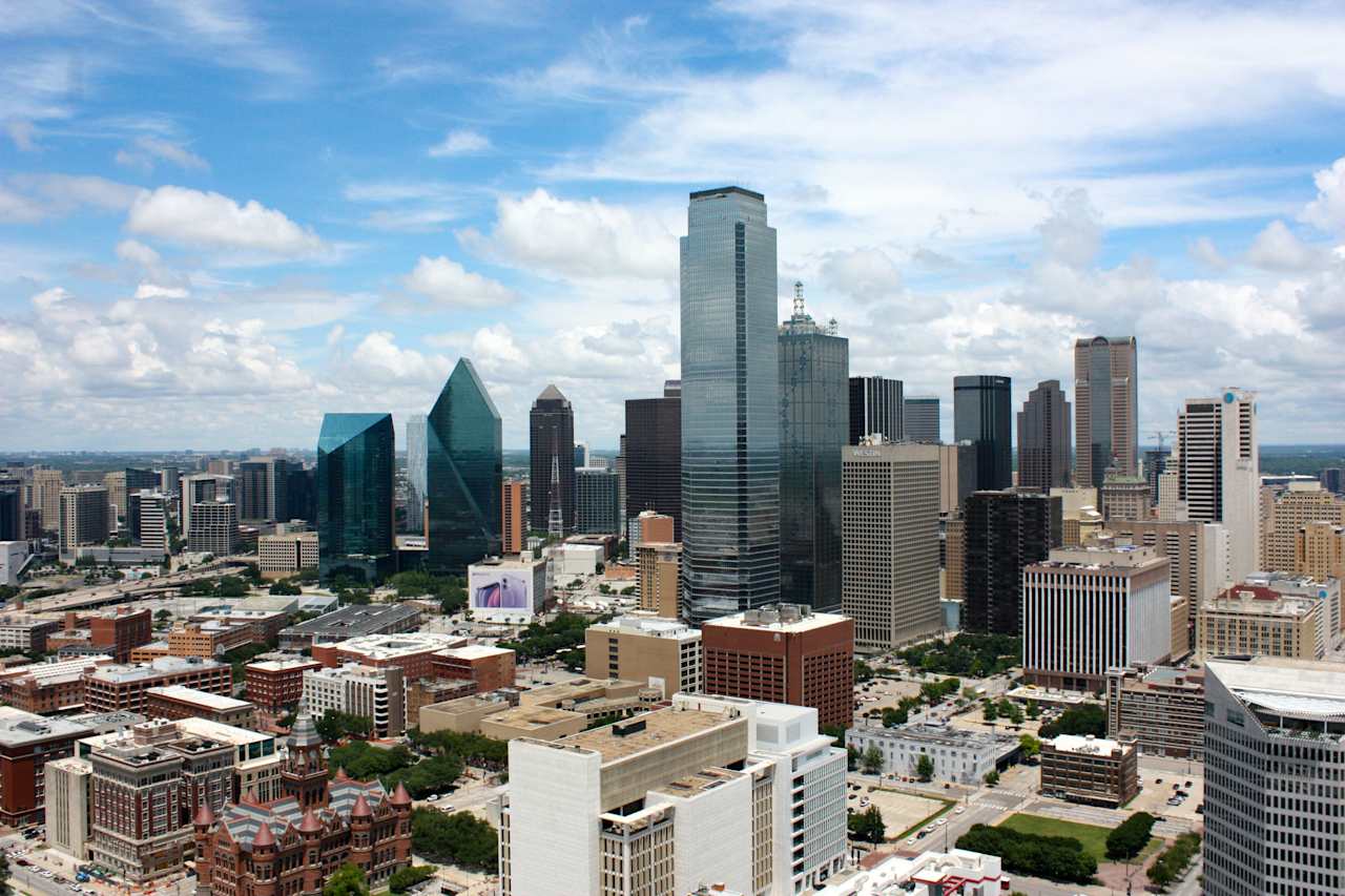 An aerial view of the Dallas skyline, featuring notable towers and the meandering Trinity River.