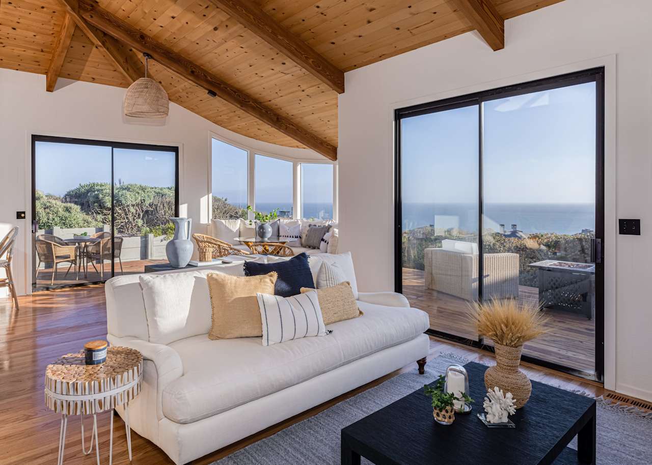 Living room with a vaulted wood ceiling, white sectional, and sliding doors overlooking the ocean.