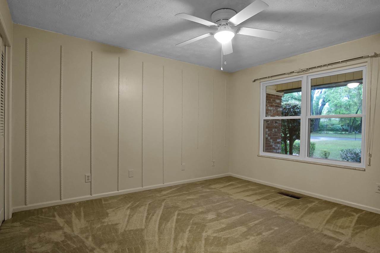 n interior view of a room with carpeted flooring, a ceiling fan, and a window providing natural light.