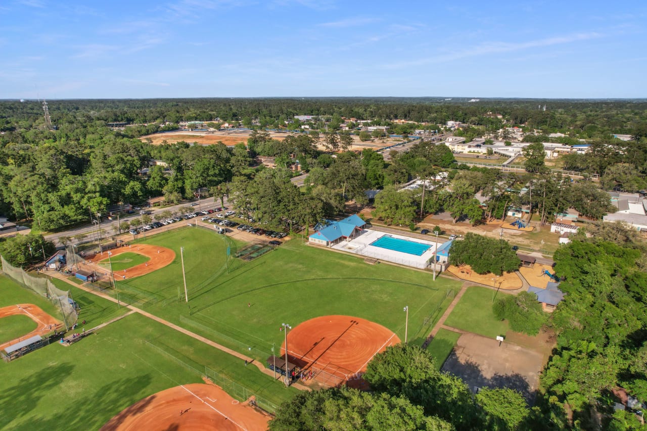 An aerial view of Levy Park, featuring a sports complex with baseball fields and a swimming pool. The area is well-maintained and surrounded by trees.