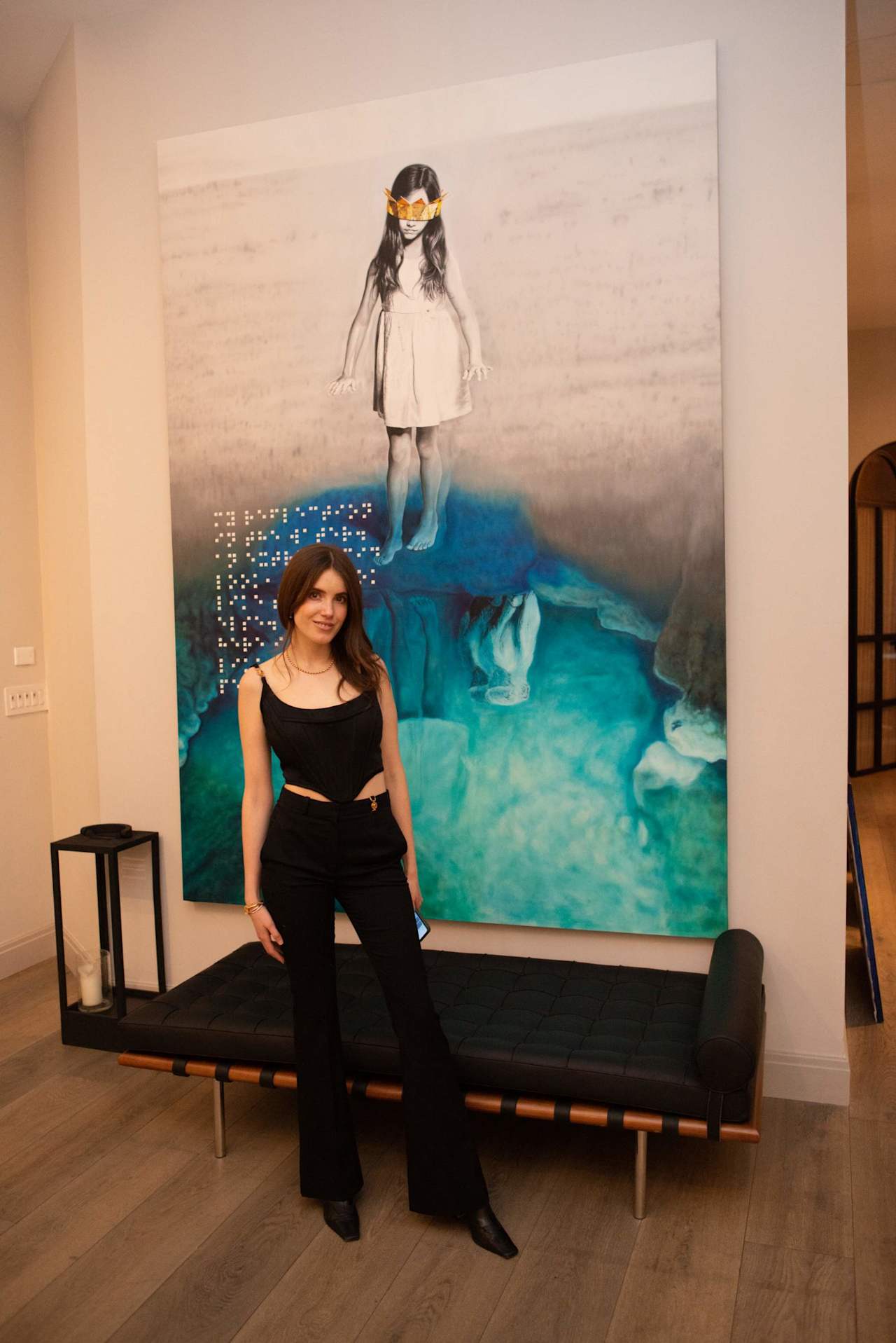 Woman in black standing before a large turquoise artwork and black bench.