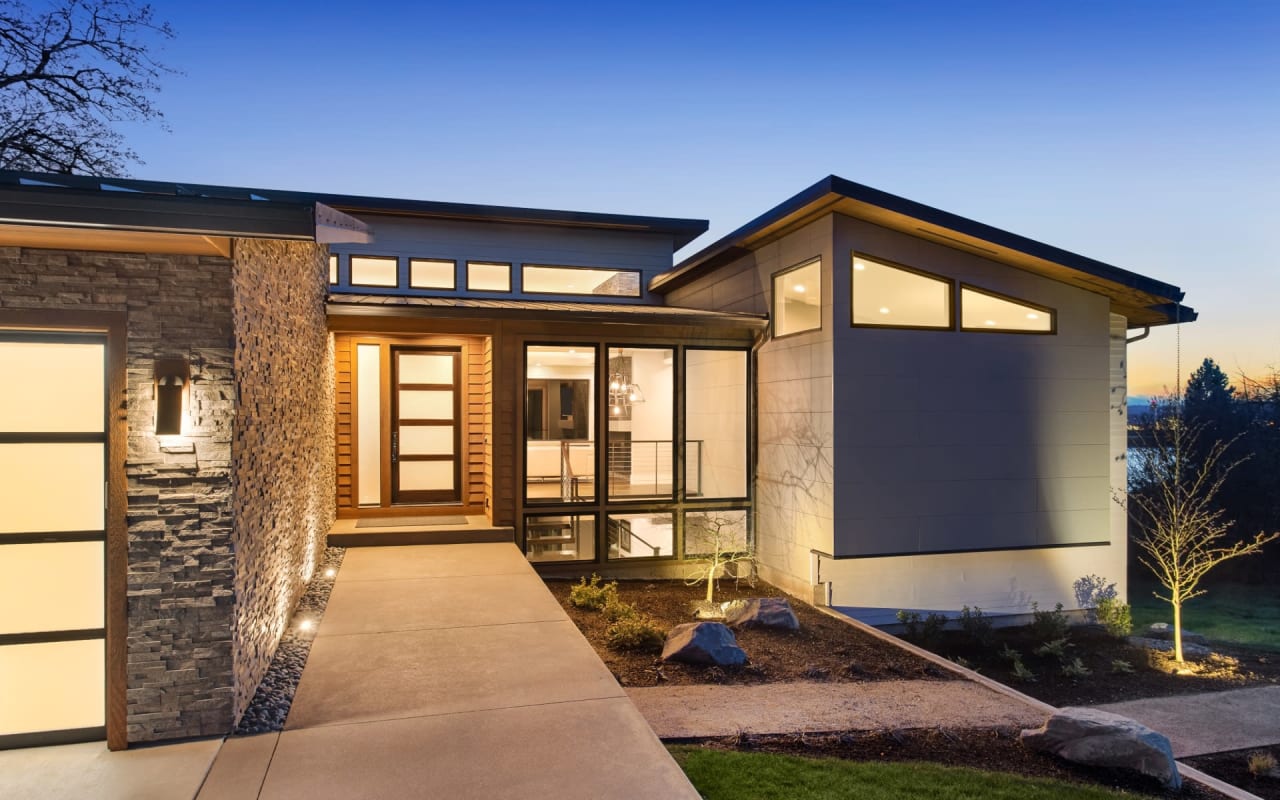 A modern house with a flat roof, large windows, and a concrete walkway leading up to the front door. 