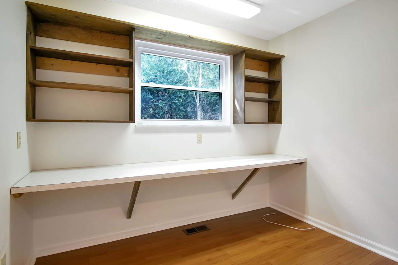 Photo of a wall in the utility room featuring built in shelving around a large window, and a built-in countertop that spans the length of the room