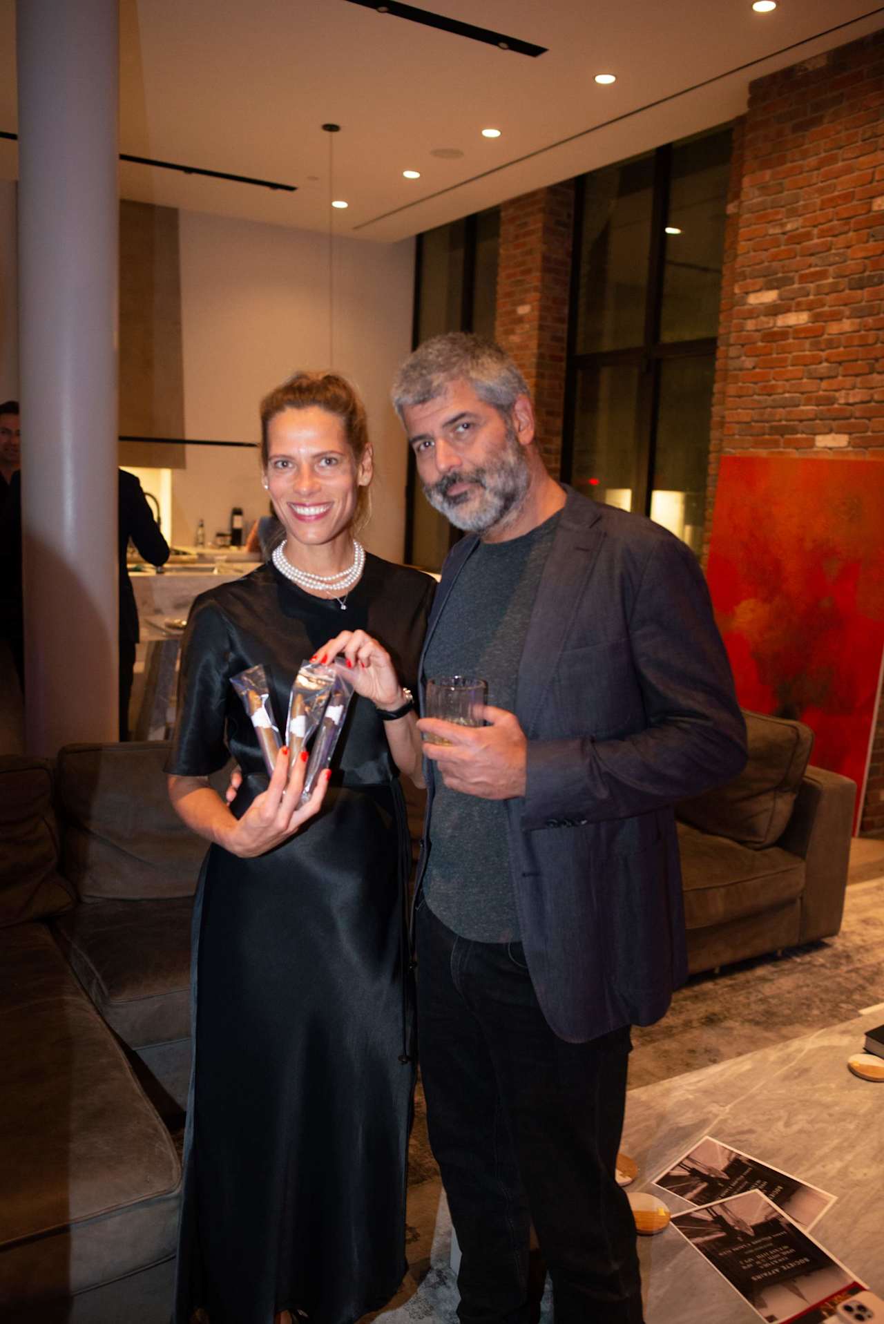 A woman holding packaged items and a man with a drink pose together indoors.
