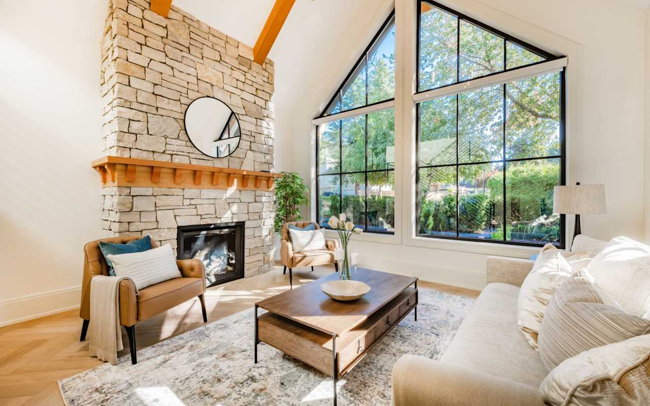 A living room with a brick fireplace, a light colored rug and a large window