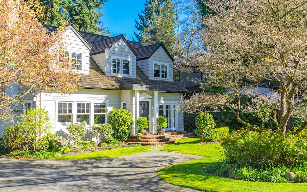 White two-story home with front dormers, brick entry steps, and a landscaped lawn.