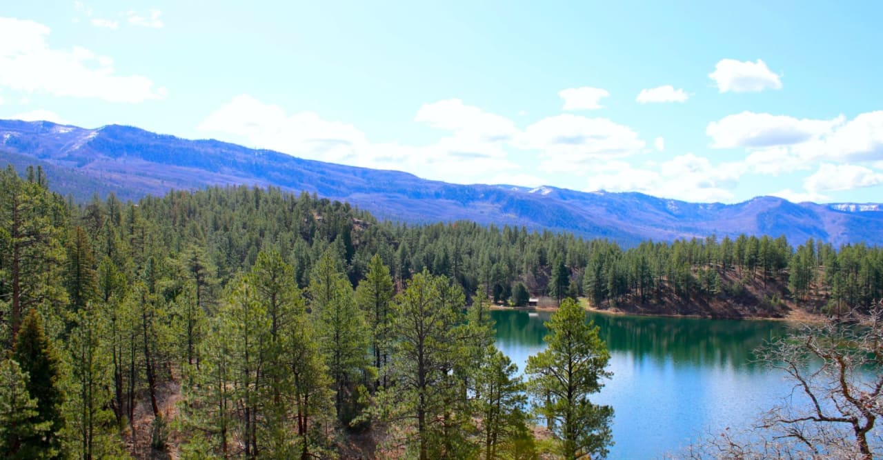 A mountain lake bordered by pine-covered hills, with distant blue ridges.