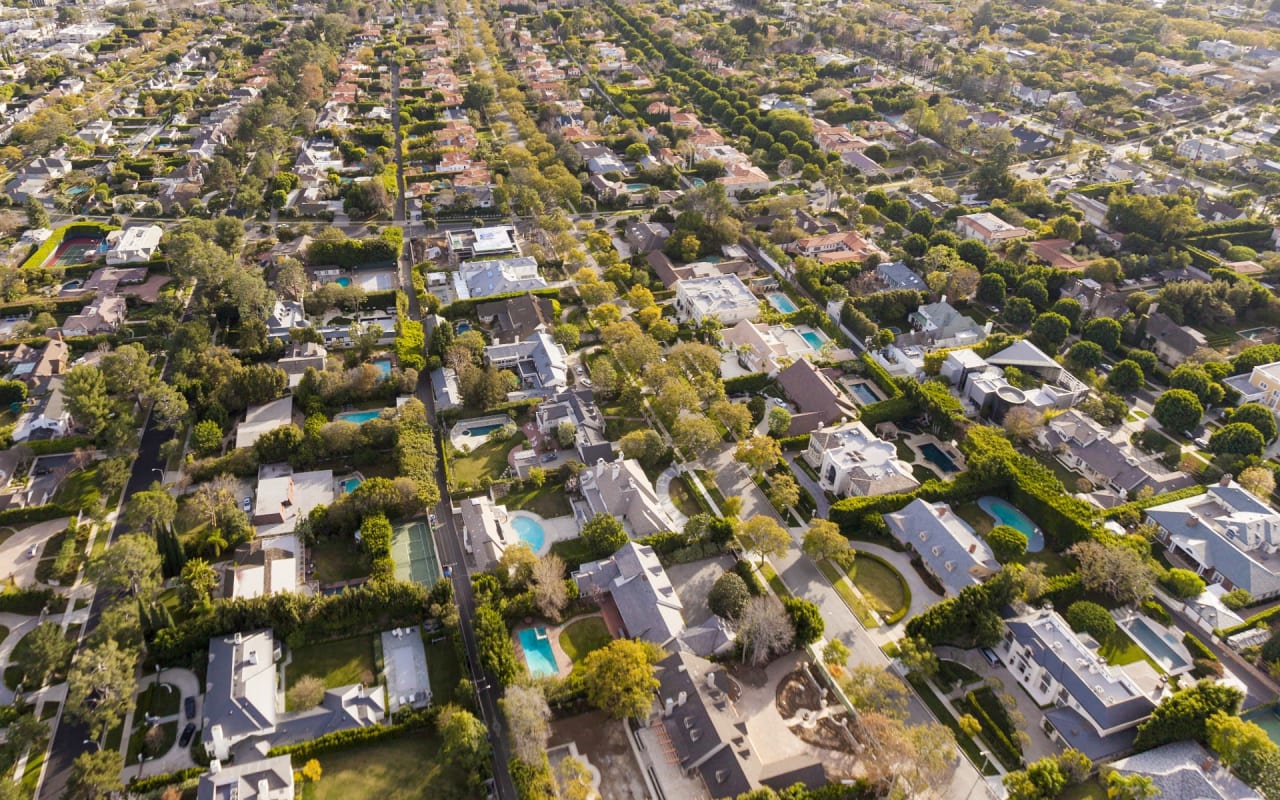 An aerial view of a residential neighborhood with lots of houses, trees, and swimming pools