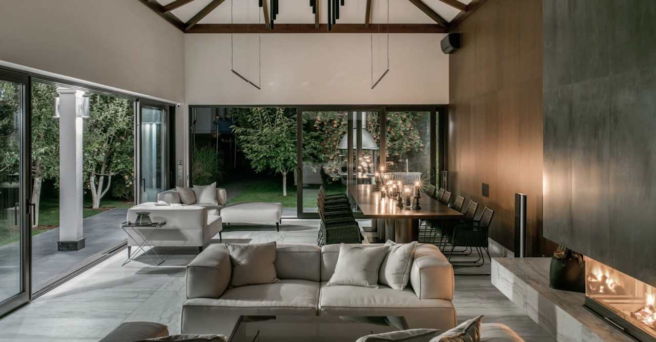 Open-plan living and dining room with vaulted ceiling, glass doors, and a lit fireplace.