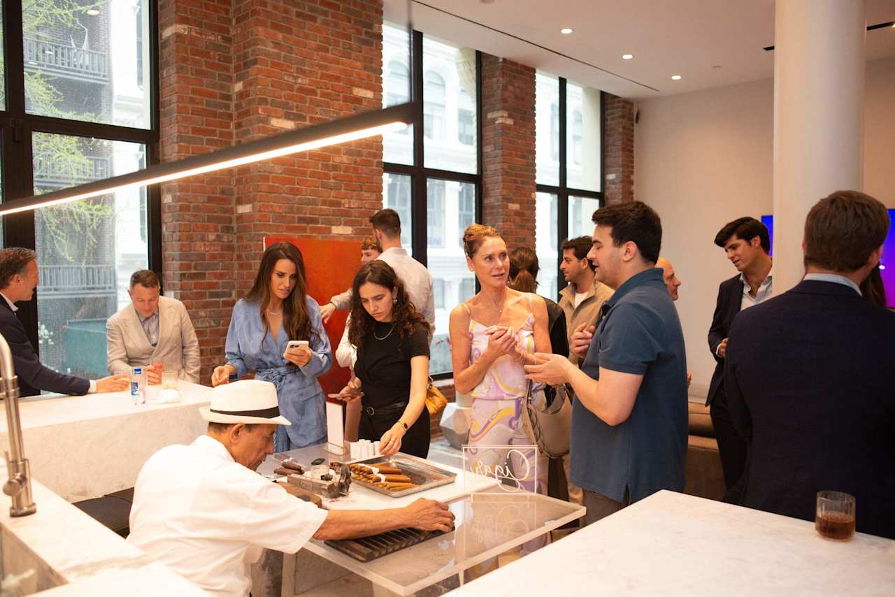 Guests mingle around a chef serving food in a bright, brick-walled event space.