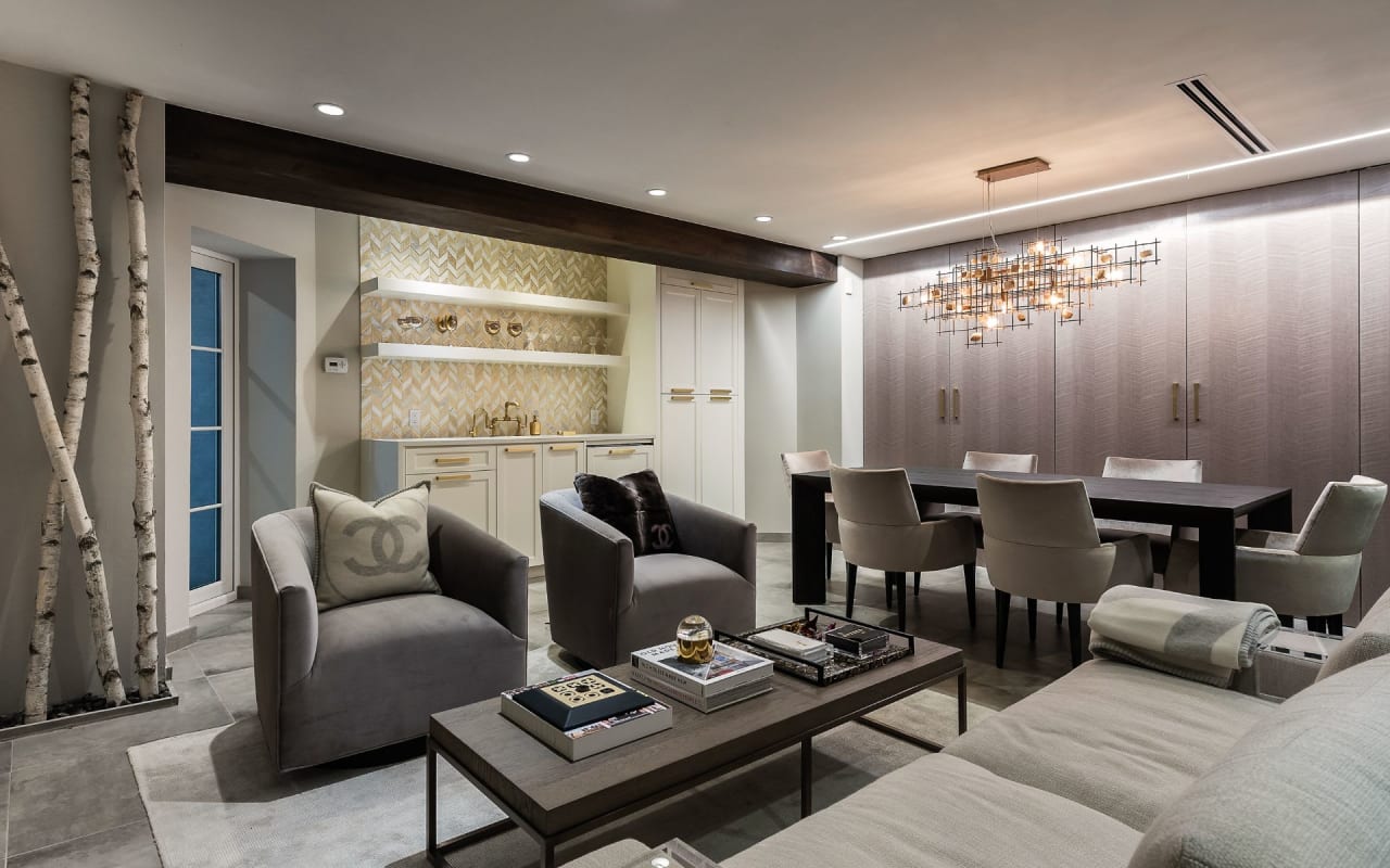 Inviting basement living room featuring a comfy couch, versatile dining area, and elegant wet bar with stylish gold hardware.