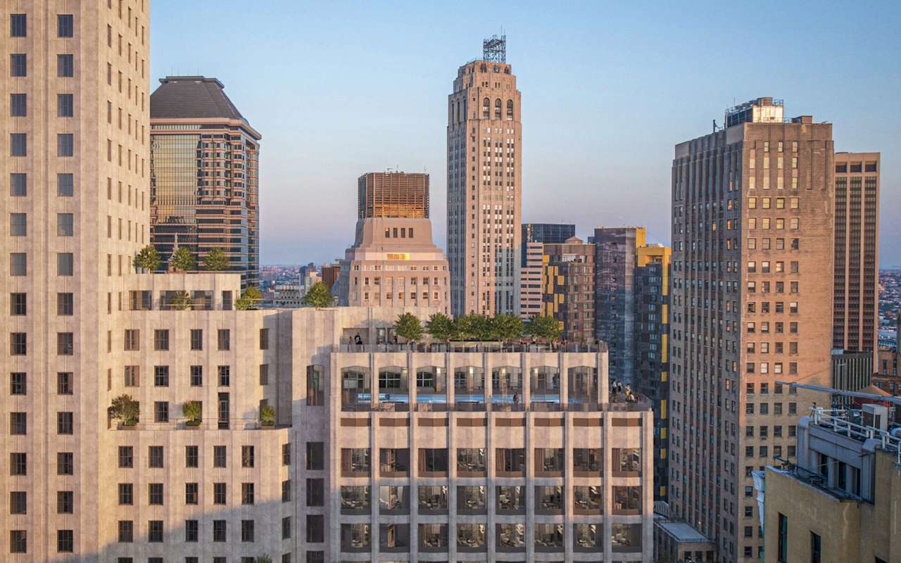 A city skyline featuring various modern and historic skyscrapers, with greenery on rooftops and a clear sky at sunset.