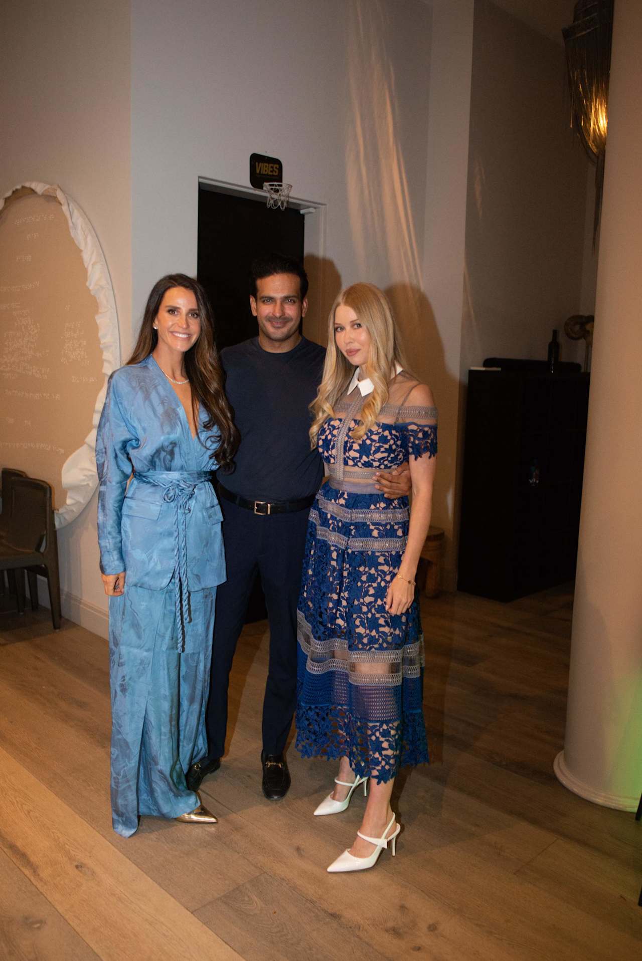 Three adults pose indoors, wearing blue outfits beside a small basketball hoop.