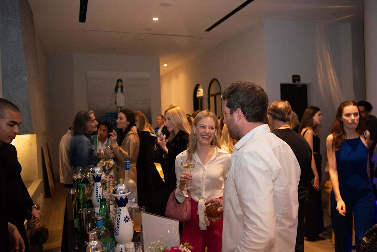 Guests mingle at a reception; a smiling woman in a white blouse chats with a man.