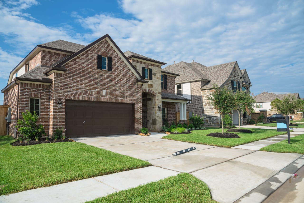 A row of diverse single-family homes with different kinds of siding, driveways to car garages, sidewalks, and front lawns.