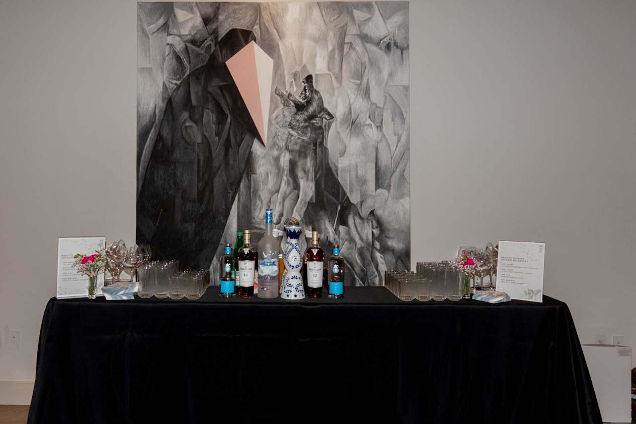 Drinks table with bottles and glassware beneath a large monochrome abstract painting.
