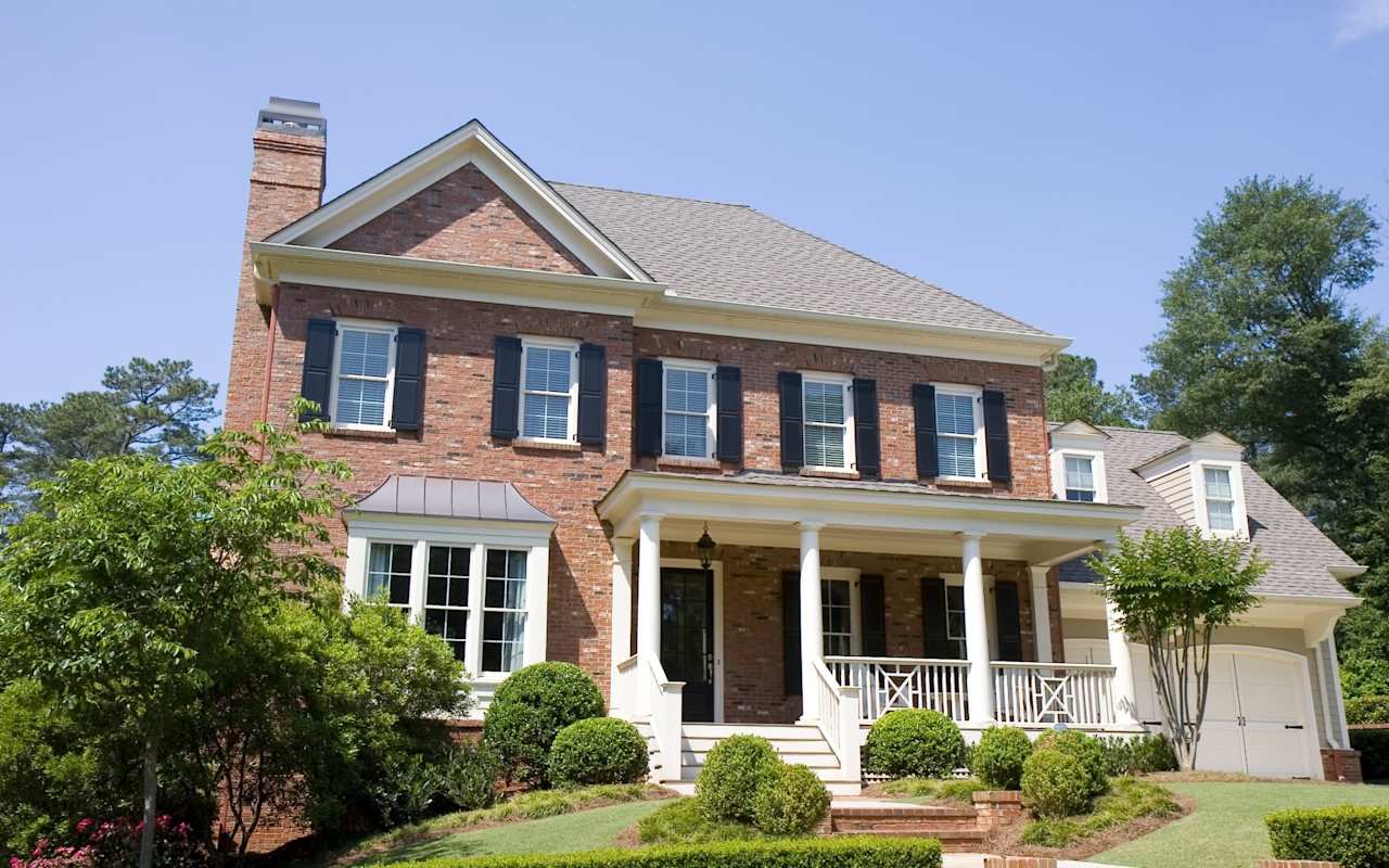 Two-story brick home with a white-columned porch, dark shutters, and an attached garage.