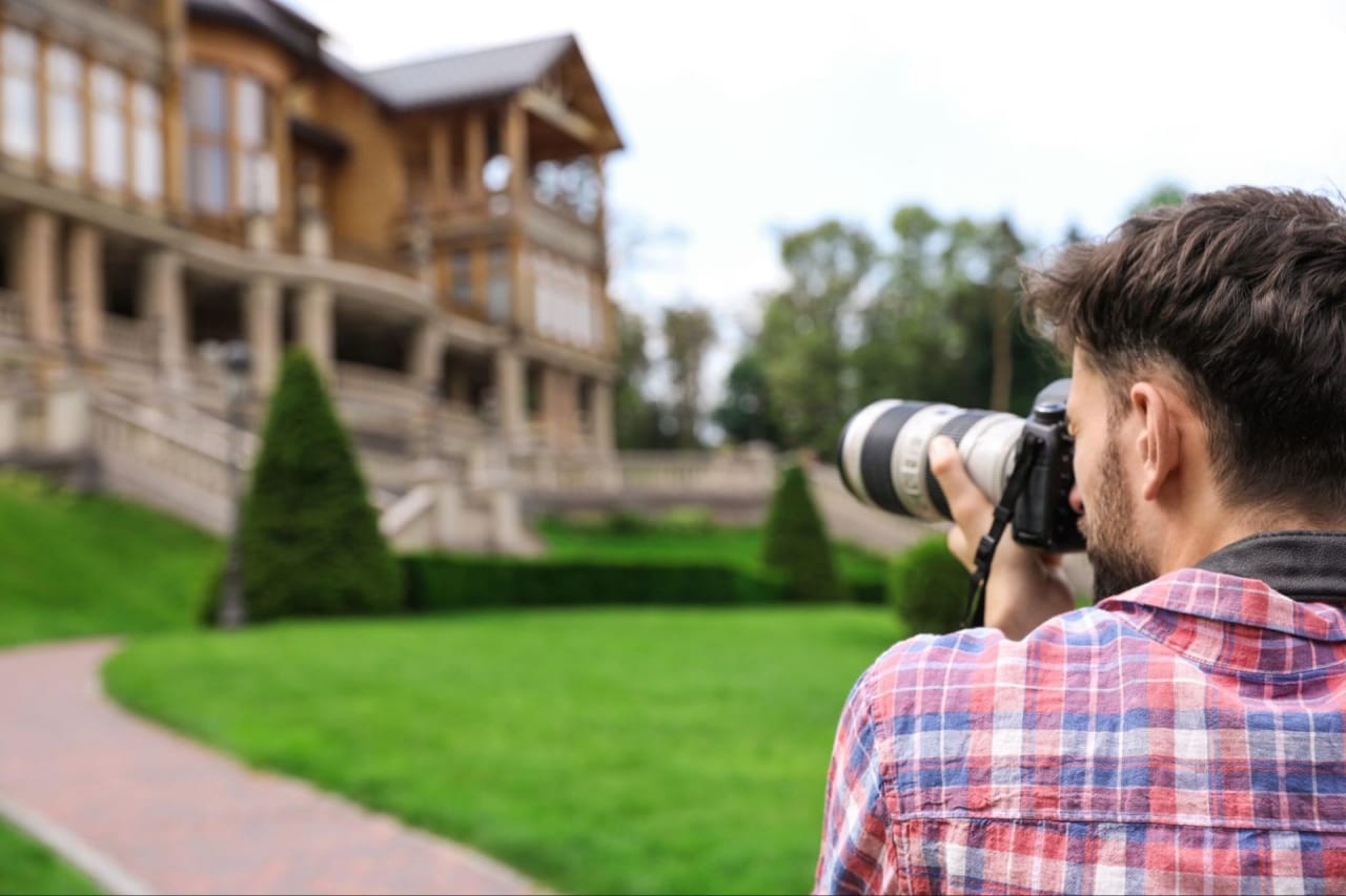 A man capturing a photograph of a beautiful house with his camera.