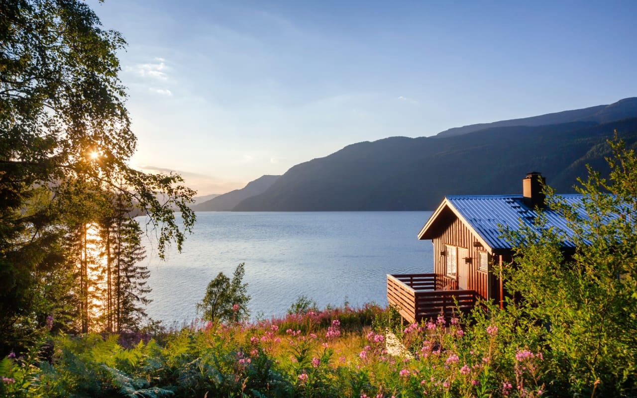 A wooden cabin with a blue roof on the shore of a lake.