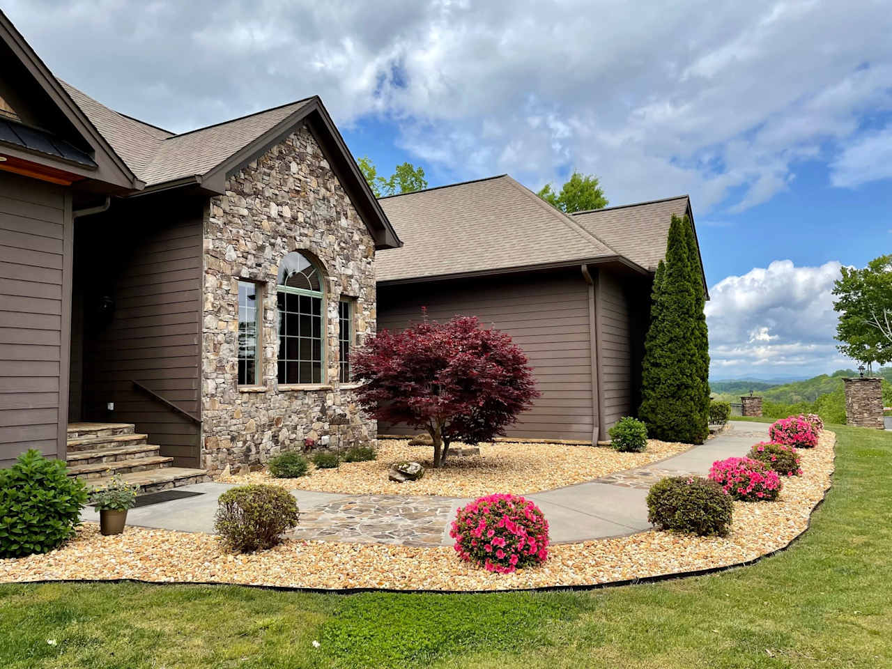 A close-up of the front of a house with a variety of colorful flowers and bushes in bloom.