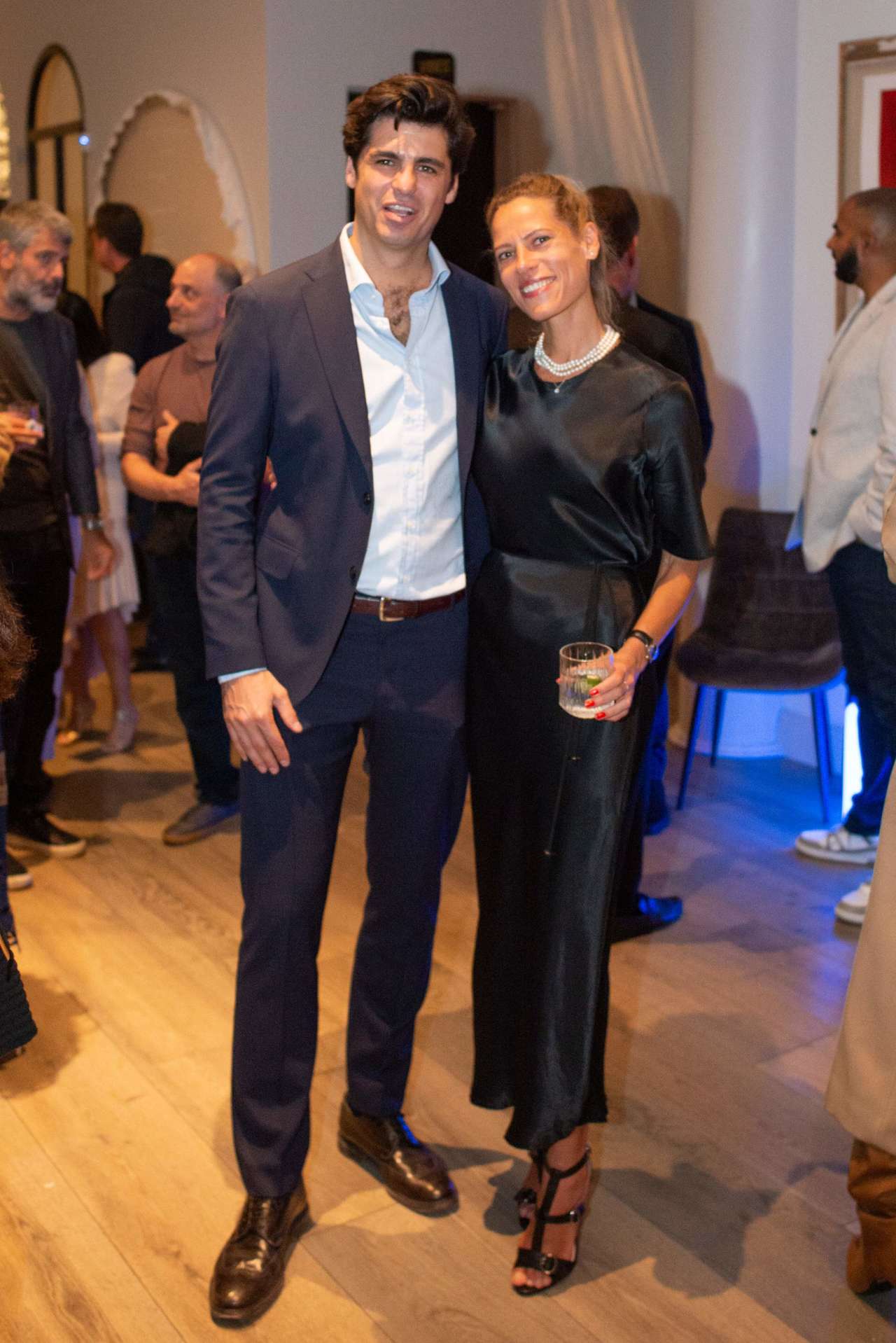 A suited man and a woman in a black dress pose together at a gathering.