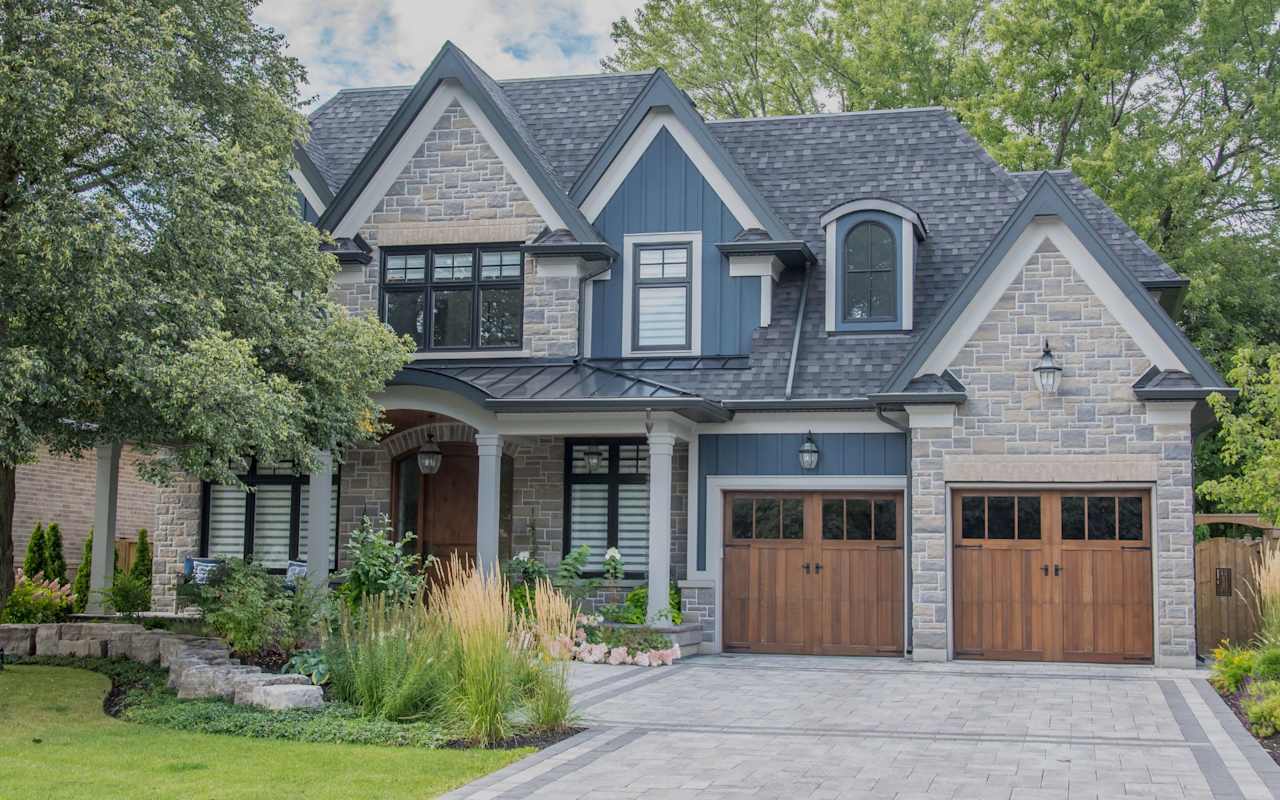 A large house with a wooden garage door, a brick driveway, and a green lawn.