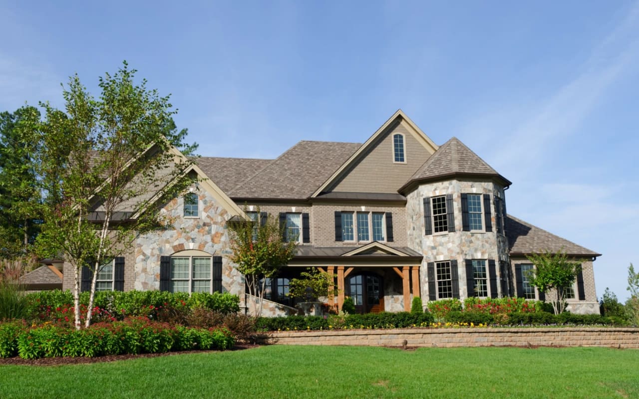 A large house with a big green lawn in front of it. It looks like an upscale suburban house.