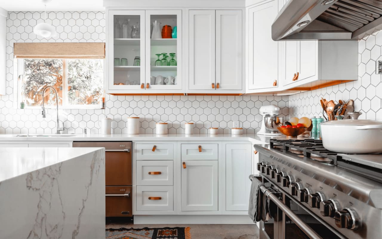 Modern kitchen with white cabinets, hexagonal tile backsplash, stainless steel appliances, and marble countertops.