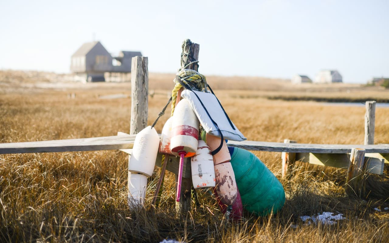 Buoys hanging from a wood fence in a grassy field in Madaket.