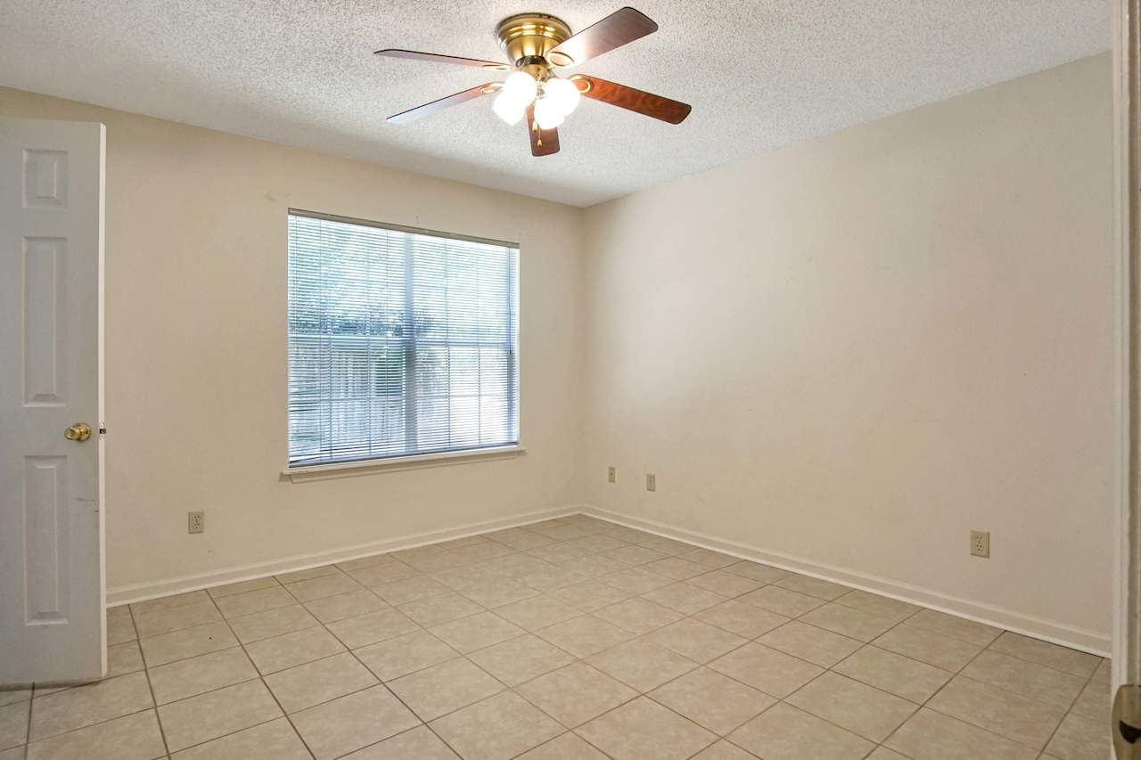 Photo of the primary bedroom featuring white ceilings, lightly colored walls, a large window with white grid and white blinds, and the door to the walk-in closet  at 2709 Oak Park Court, Tallahassee, Florida 32308