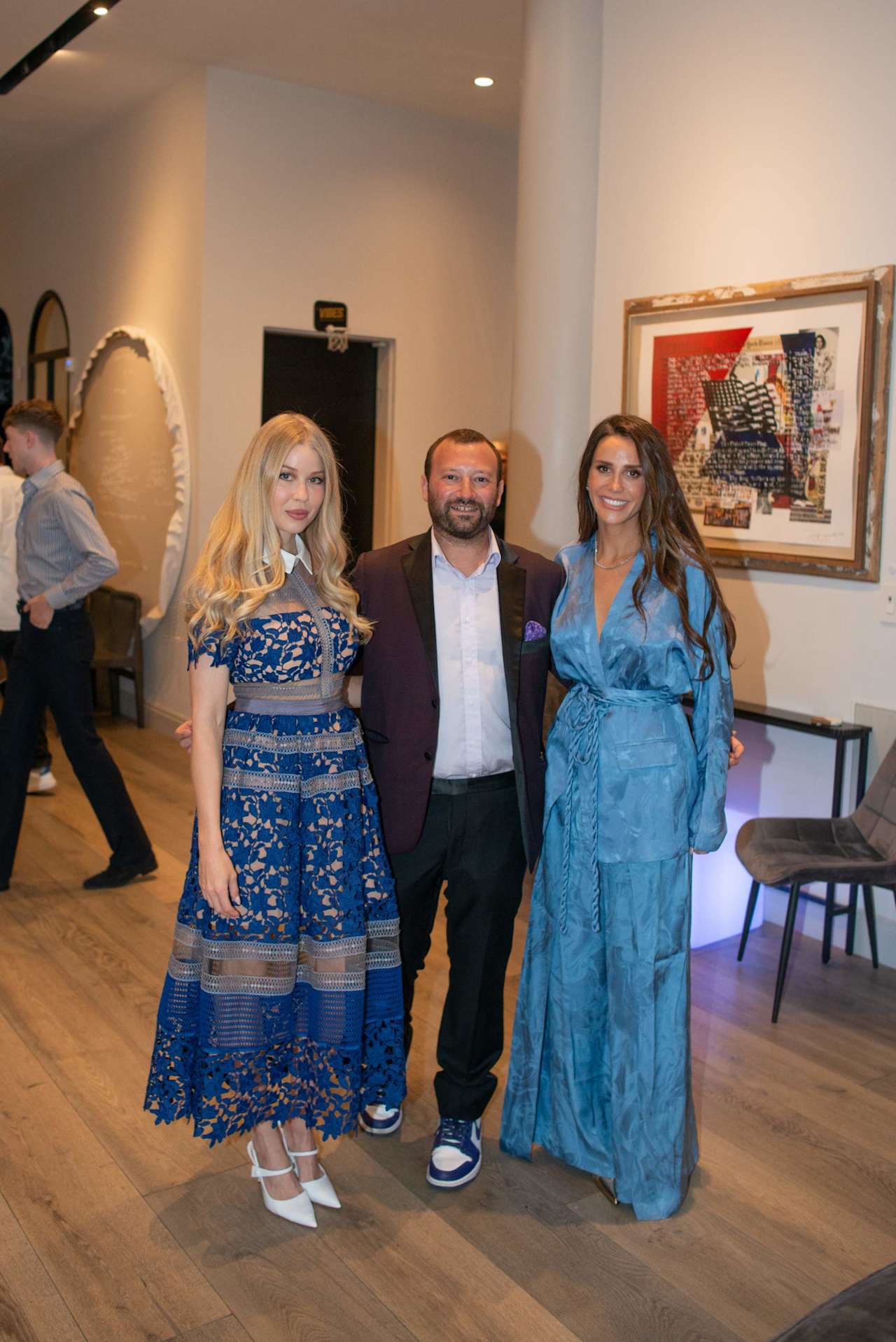 Three event guests pose together in blue outfits inside a gallery-like room.