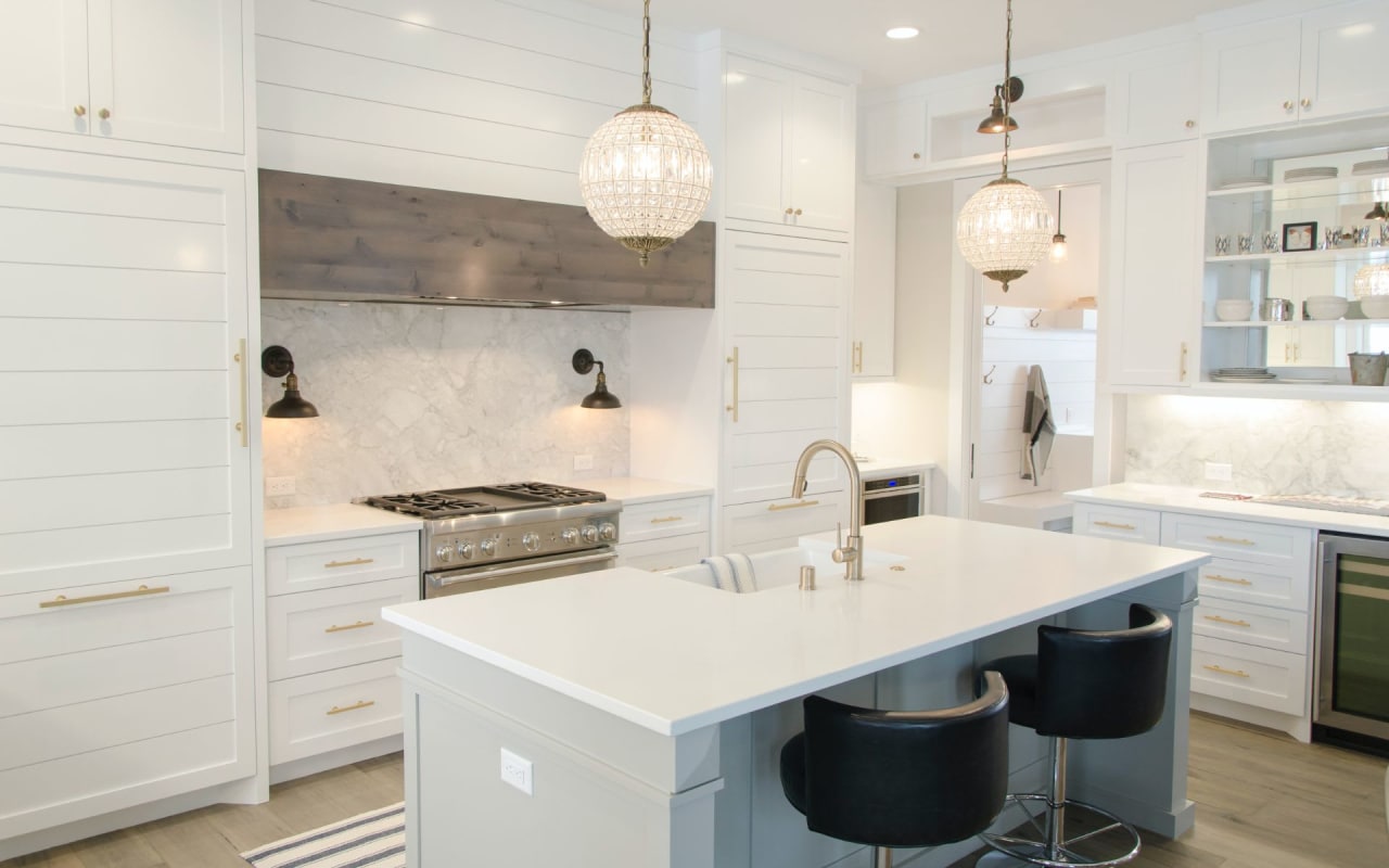 A modern kitchen with a marble backsplash, a center island, pendant lights, cabinets, and stainless steel appliances.
