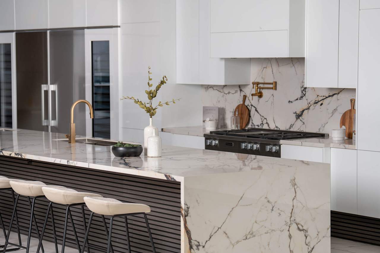 A modern kitchen with a sleek white marble countertop and white stools