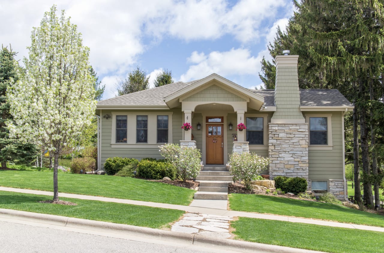 A residential house with a chimney and a leafy tree in the front yard.