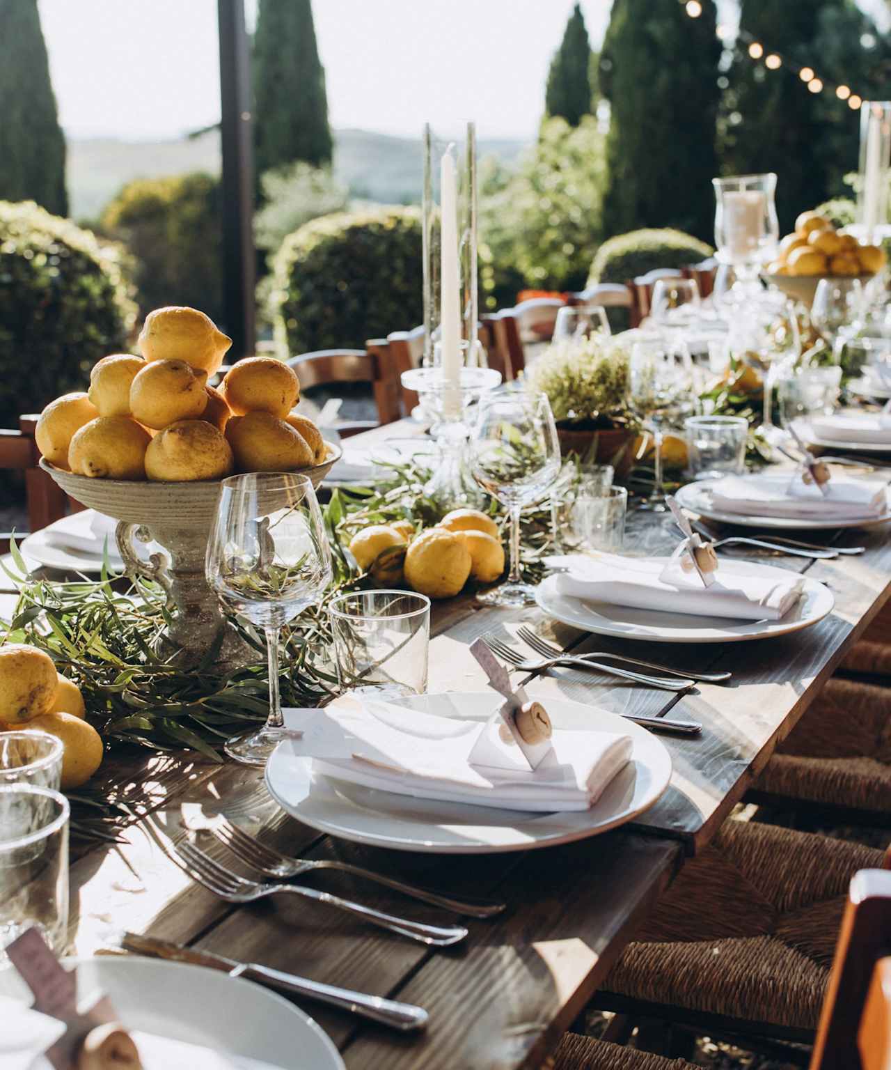 A long wooden table set with plates, glasses, and whole lemons in a fruit bowl.