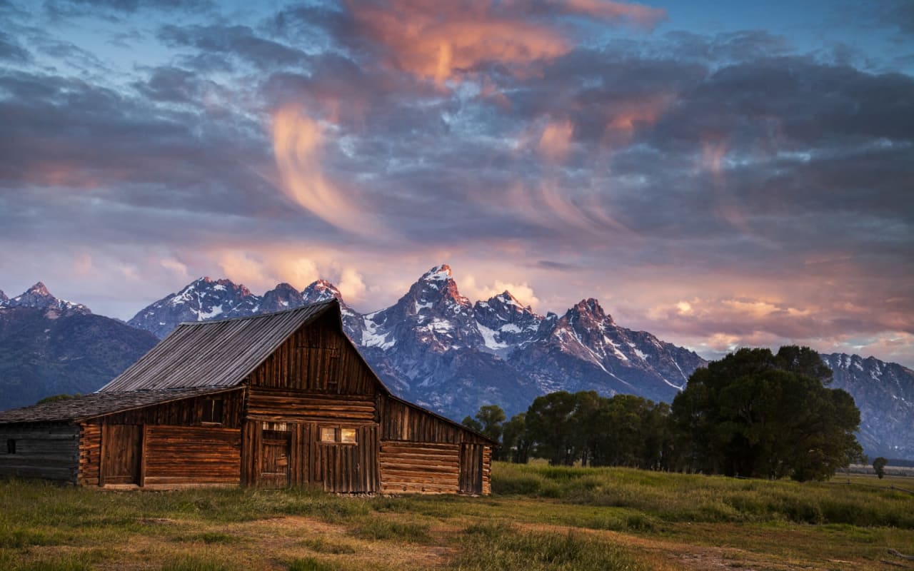 A wooden barn in a field with mountains in the background.