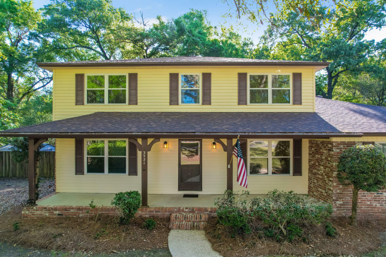 A view of the two-story house with a yellow exterior showcasing the front entrance and landscaping.