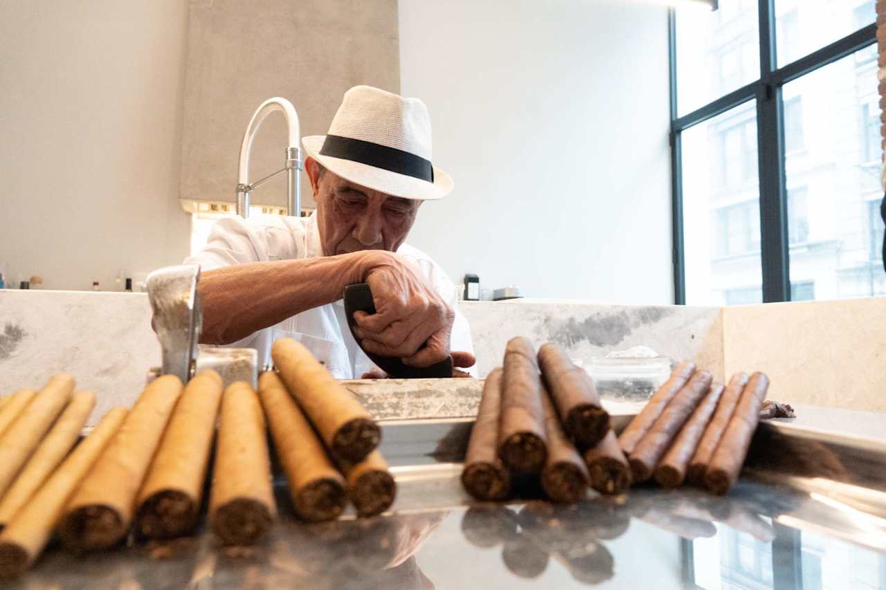 Cigar maker rolling cigars behind rows of finished cigars.