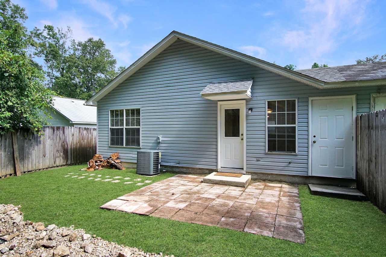 photo of rear of home featuring hardscaping, back pavered patio, outdoor storage closet, white window grids, and green grass at 2709 Oak Park Court, Tallahassee, Florida 32308