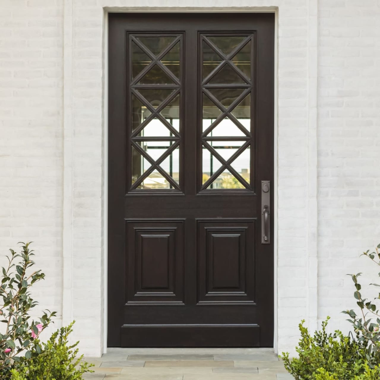 A black front door with a geometric pattern in a white brick wall. 