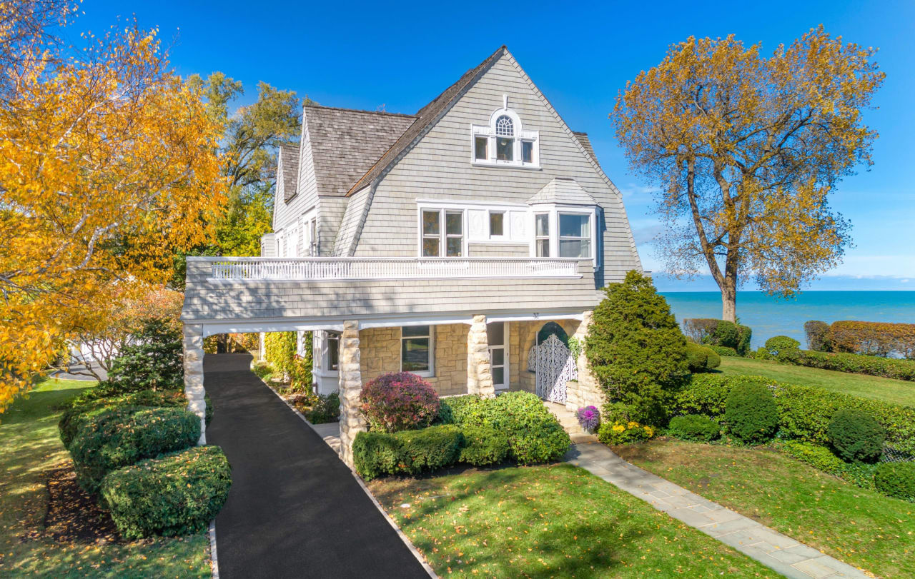 a luxury home with driveway surrounded with lush greenery and with an ocean in the background