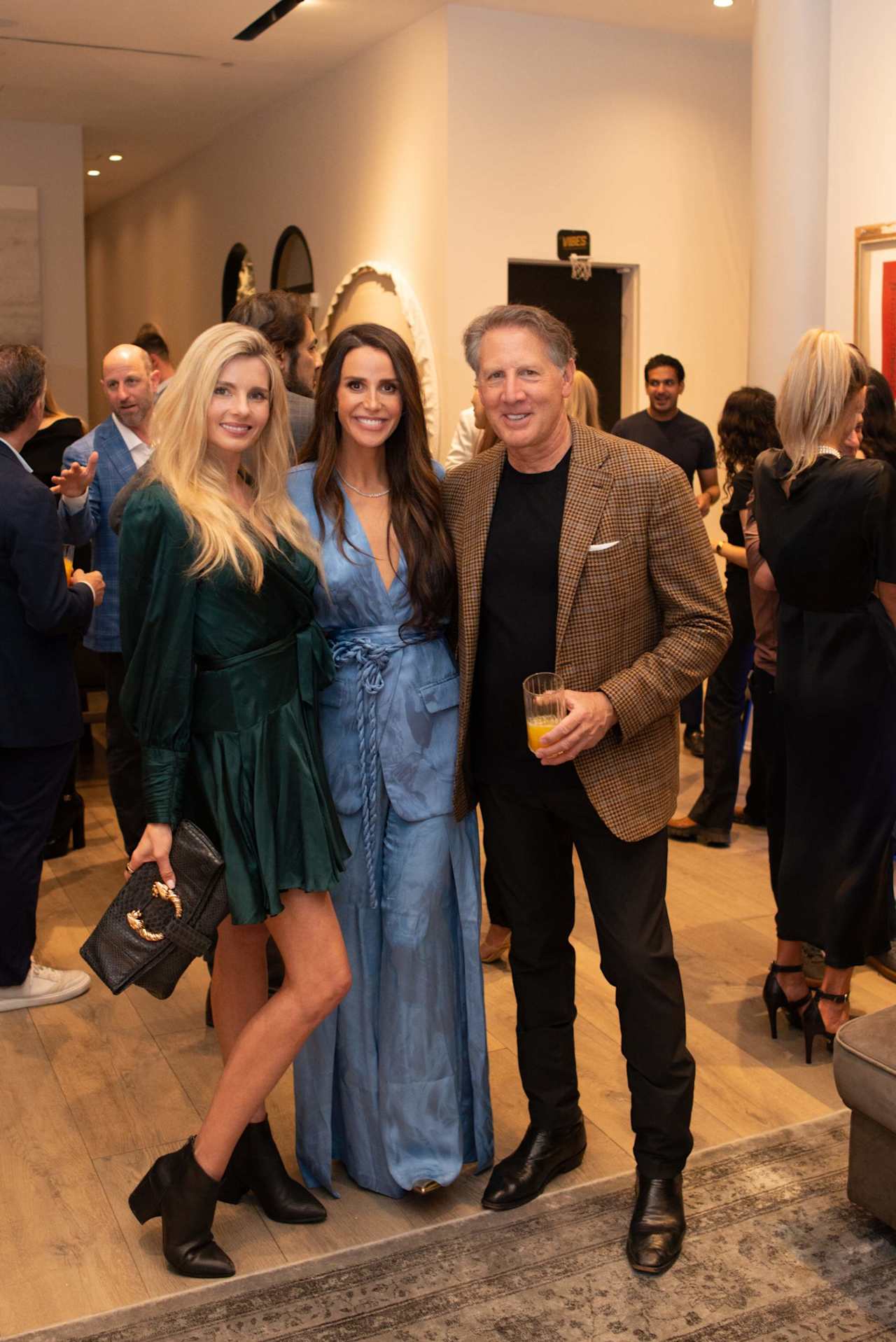 Three guests pose together at a crowded indoor reception.