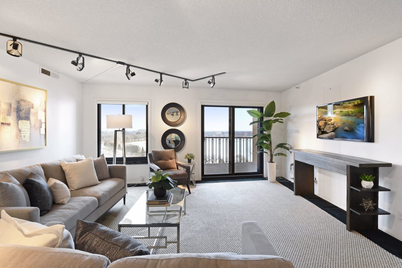 A living room with a couch, coffee table, chairs, and a flat-screen TV on the wall.